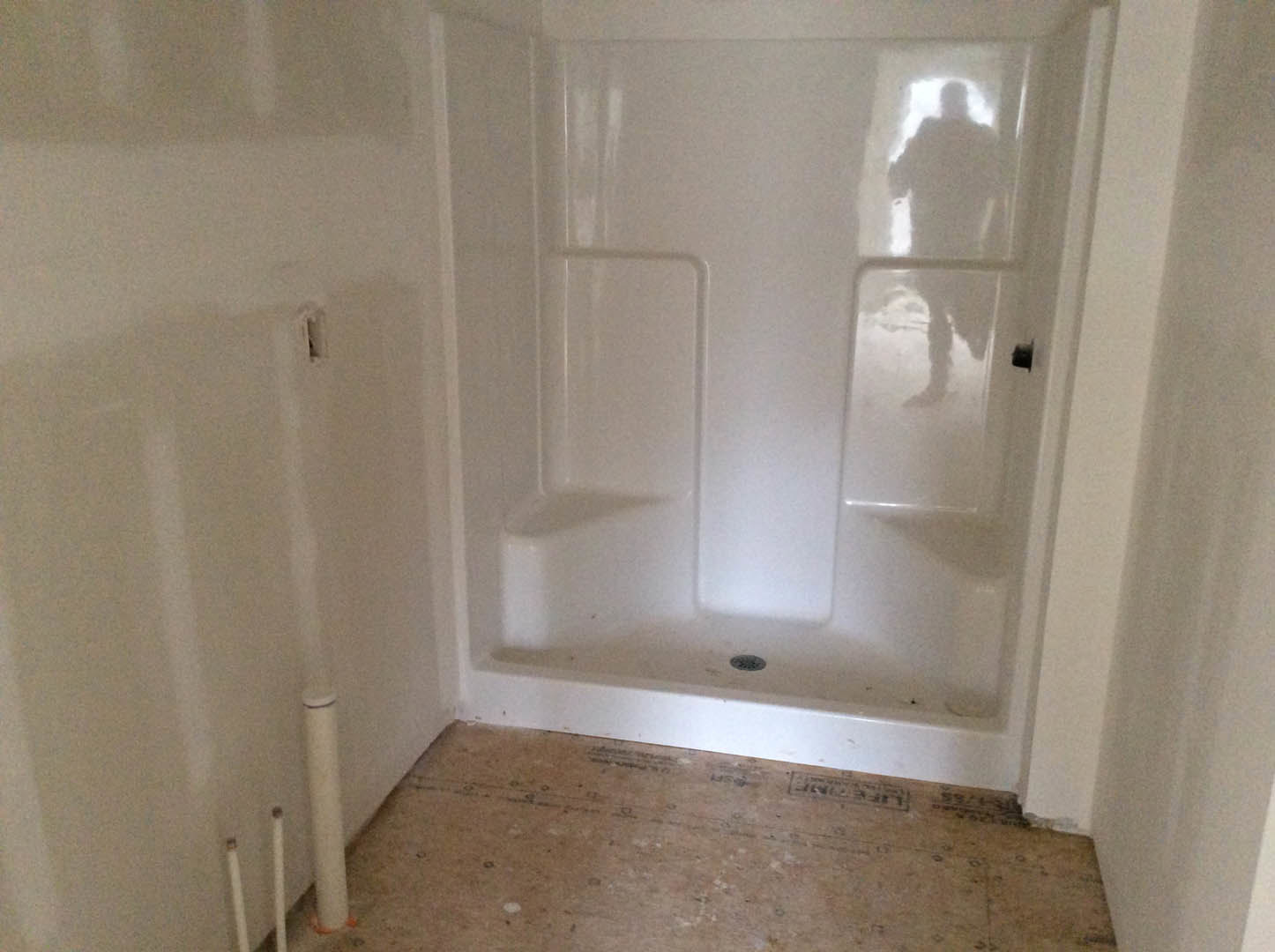 White plaster shower with glass door reflecting a blurred person, adjacent to smooth white walls and light flooring in a modern bathroom.