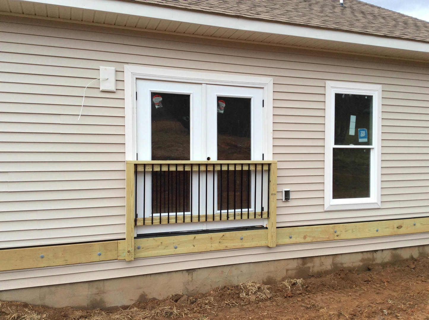 Two-story home with light siding, white double doors, balcony with metal railing, large sash windows, and covered porch.