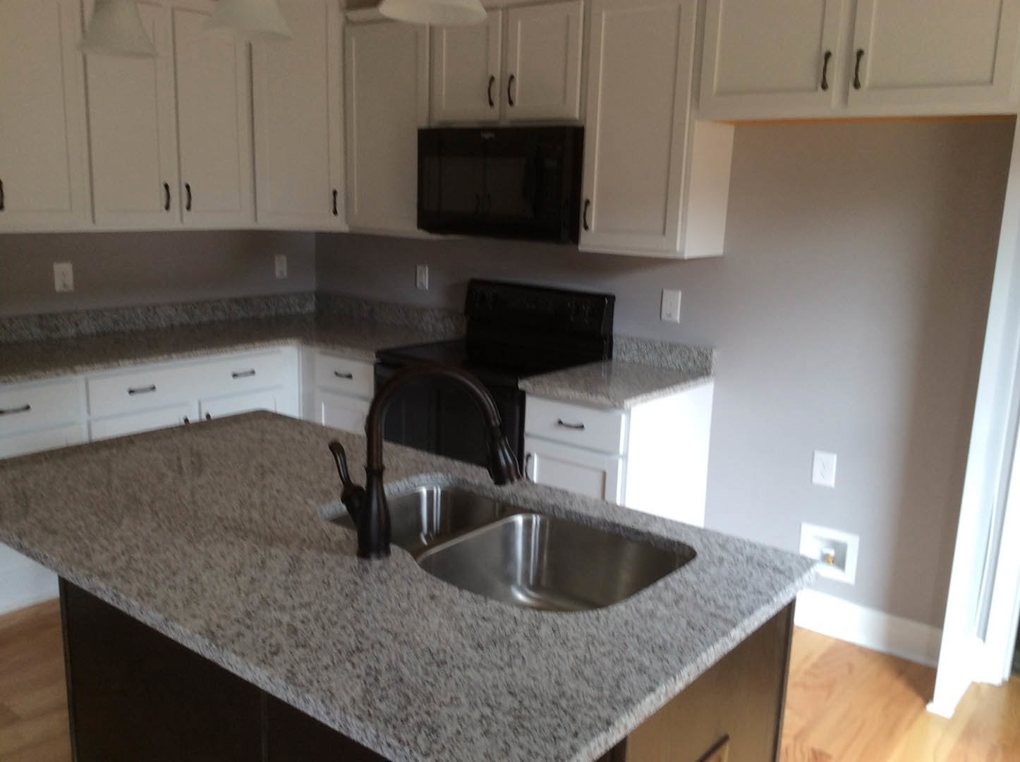 Modern kitchen with white cabinets, black microwave, granite countertops, stainless steel sink and faucet, black stove, and black cabinet accents against a white wall