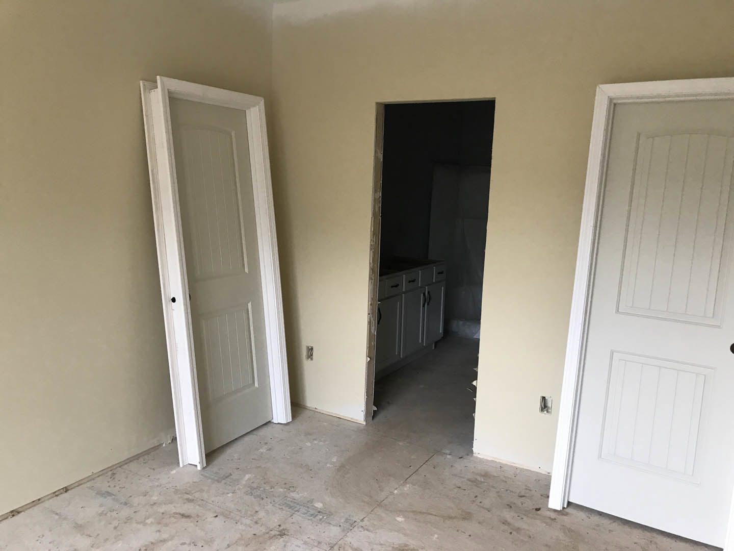 Open kitchen with white cabinetry, concrete flooring, two white doors with black handles, and smooth white plaster walls
