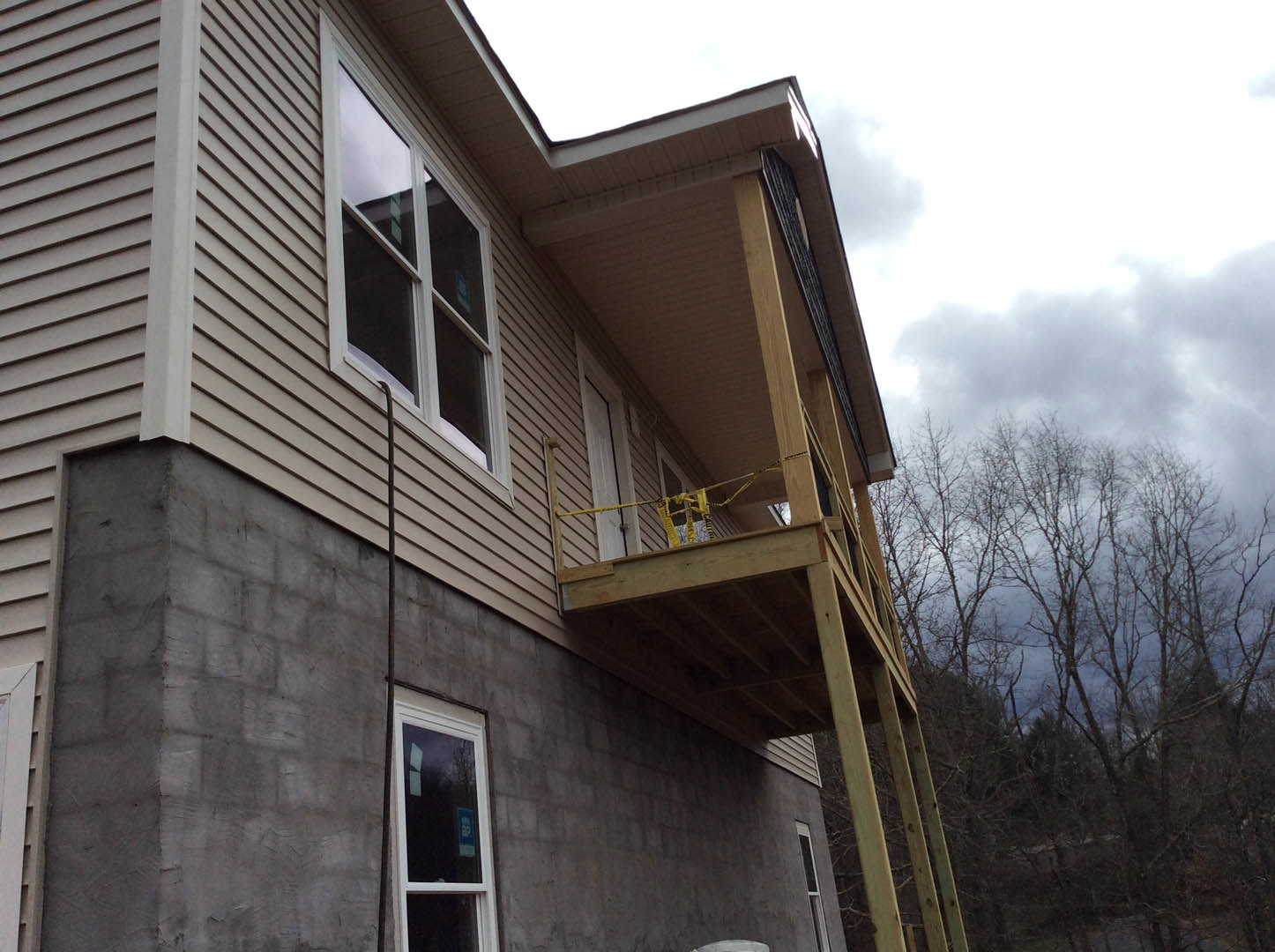 Two-story home with white siding, balcony with metal railing, sash windows, gable roof, and mature tree branches in foreground