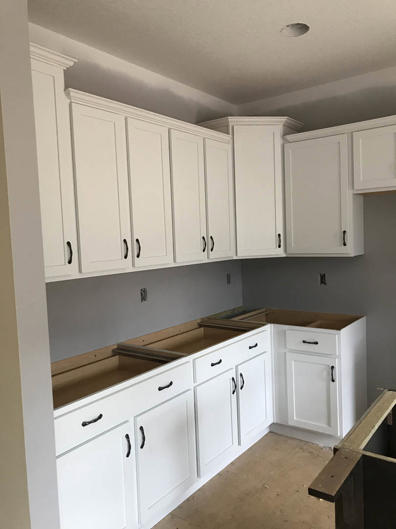 White kitchen with shaker cabinets, black handles, wood plank flooring, quartz countertops, stainless steel appliances, and a white door with matching trim.