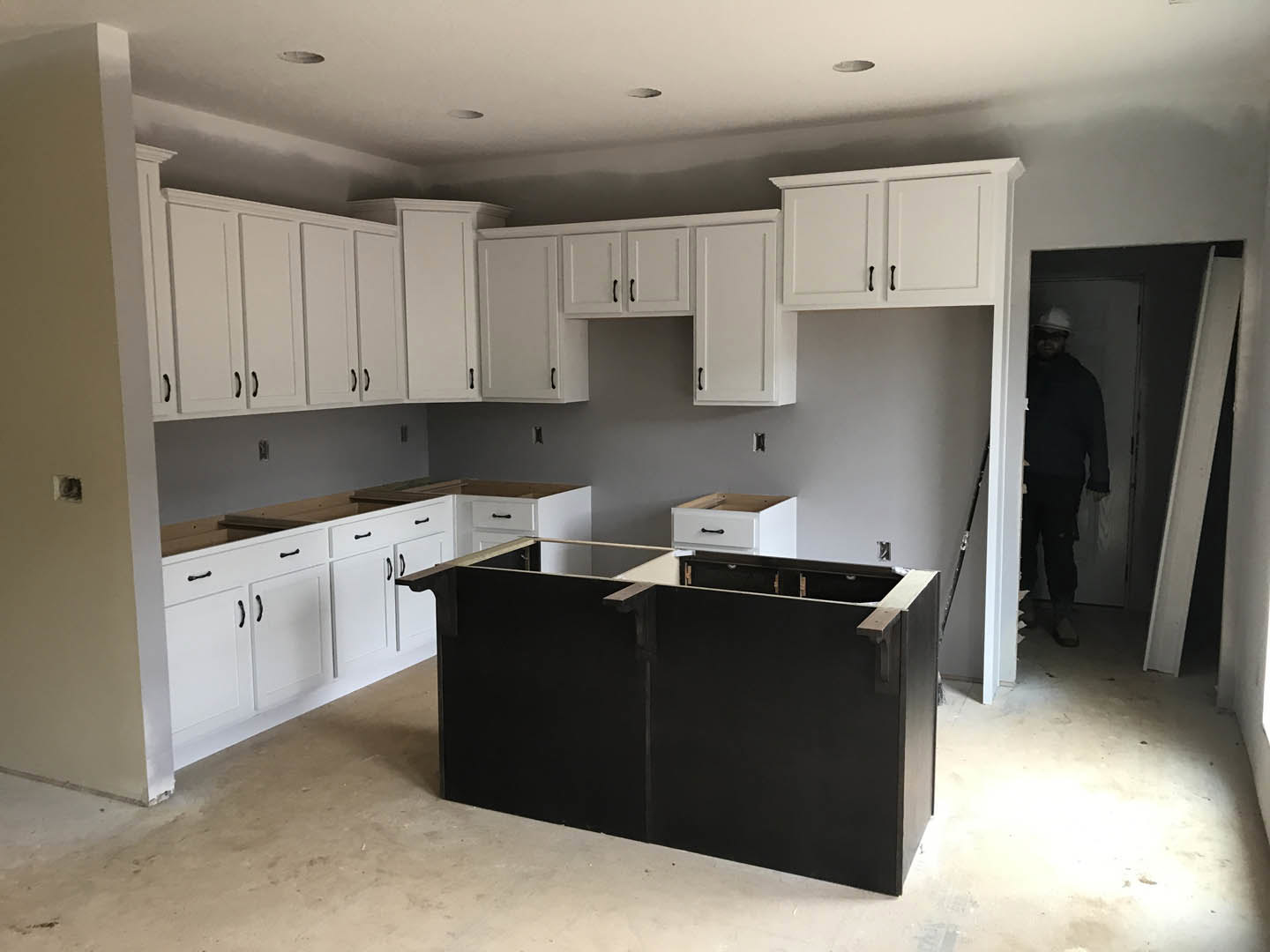 White kitchen cabinets and black island with waterfall countertop, light wood flooring, stainless steel appliances, open shelving, and recessed lighting.