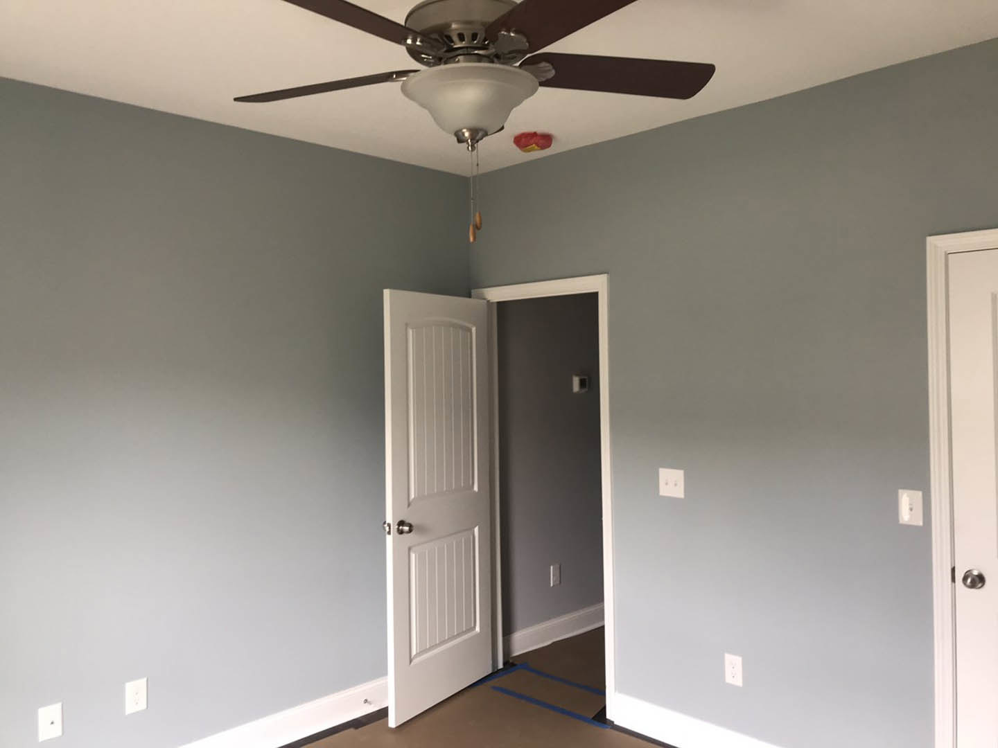 White paneled door set in a white wall, ceiling fan with light fixture overhead, neutral flooring, simple modern finishes
