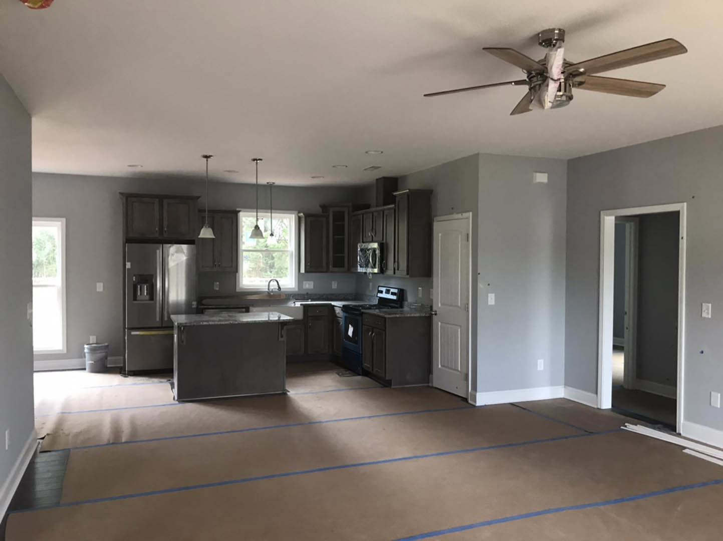 Kitchen with wood cabinetry, ceiling fan featuring a paper bag attached, white bucket with lid on floor, black rectangular appliance, black and white tiled backsplash, blue tape
