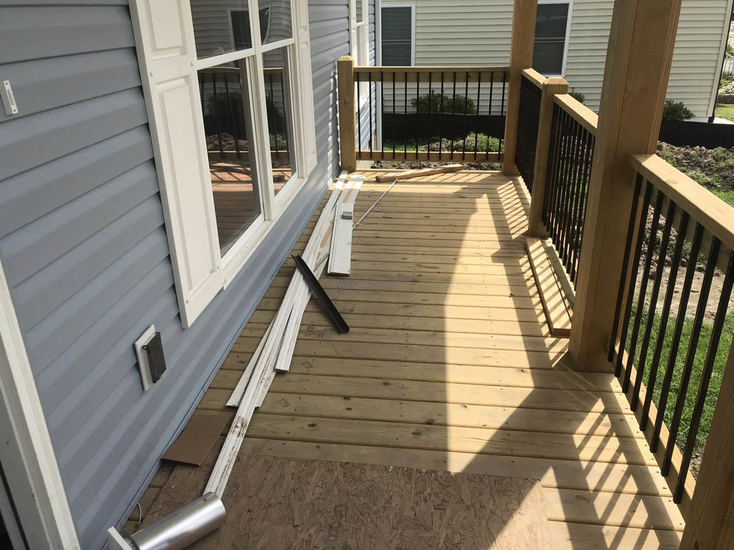 Wood plank deck with black metal railing, grey house siding, and outdoor stairs.