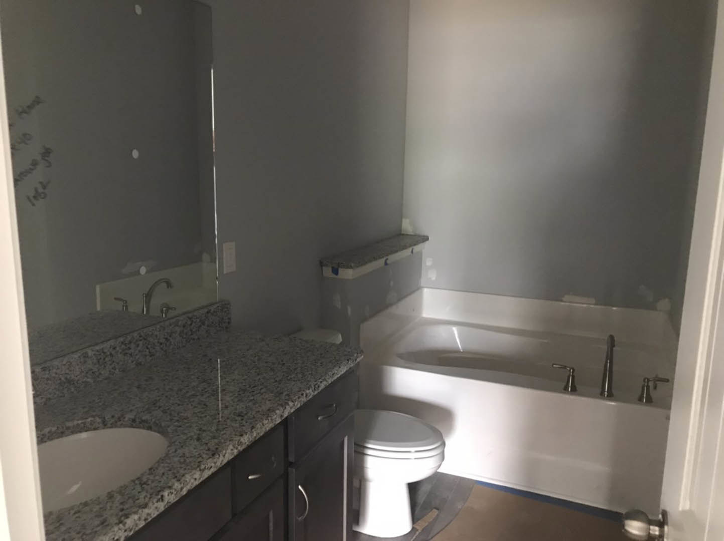 Modern bathroom featuring a freestanding white bathtub, rectangular sink set in a light stone countertop, white toilet with closed lid, and grey bench; walls finished with large