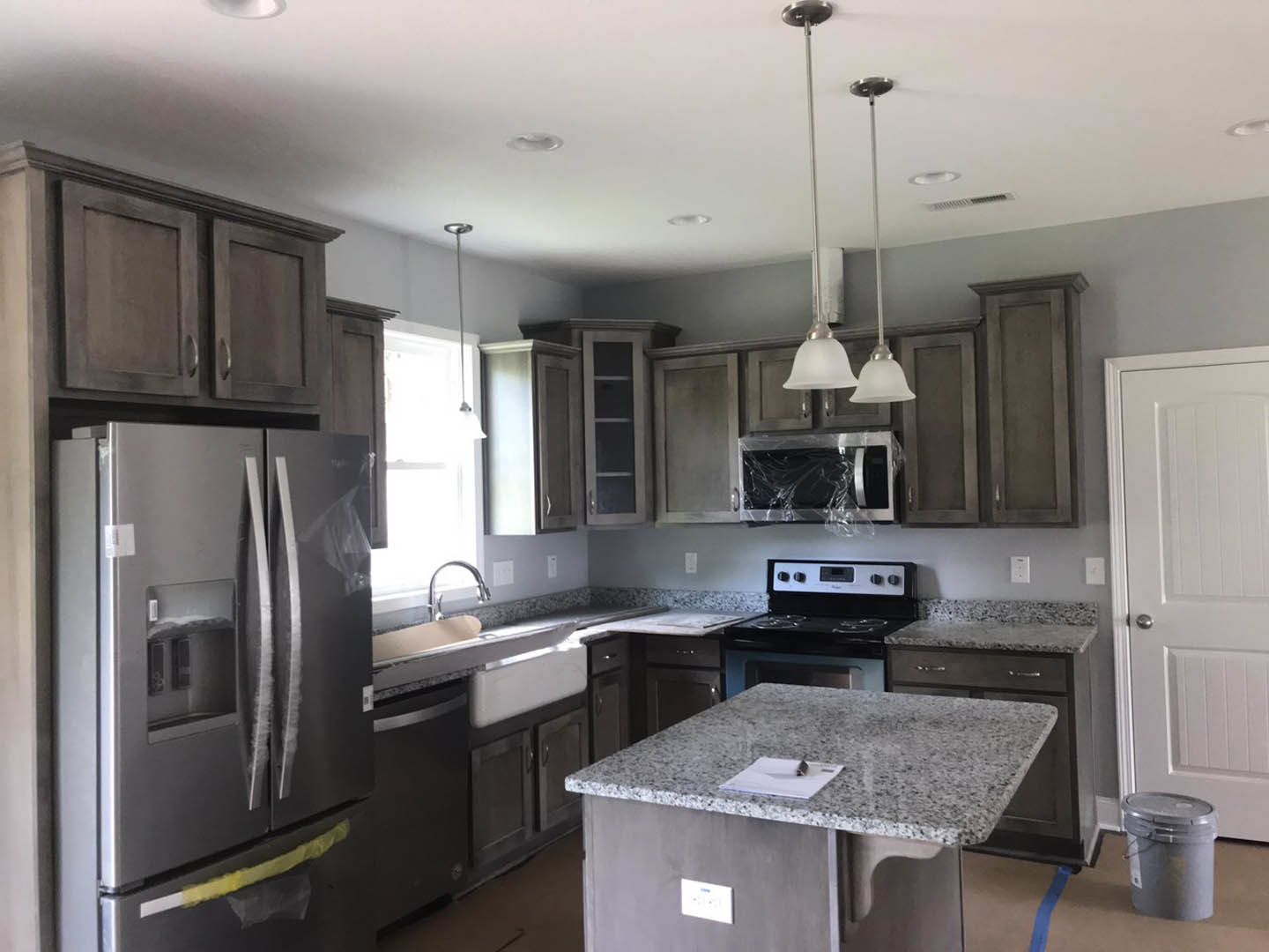 Granite countertops with undermount sink, stainless steel double-door refrigerator, stove with digital display and knobs, grey lidded bucket, paper on counter, white cabinetry