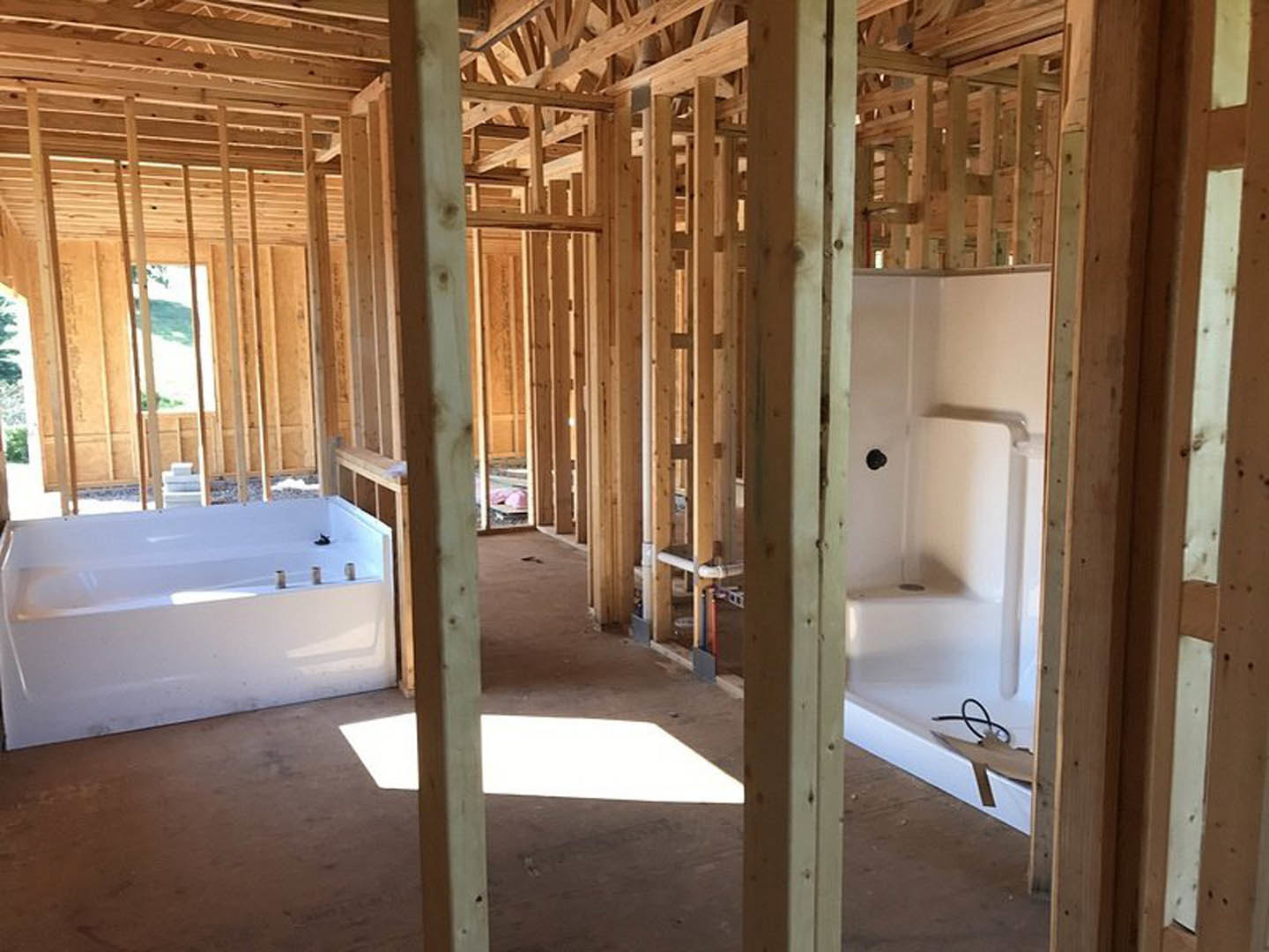 Bathroom under construction with exposed wood beams, white bathtub partially installed, scattered screws, white rectangular light fixture, stack of white boxes, and black wire on