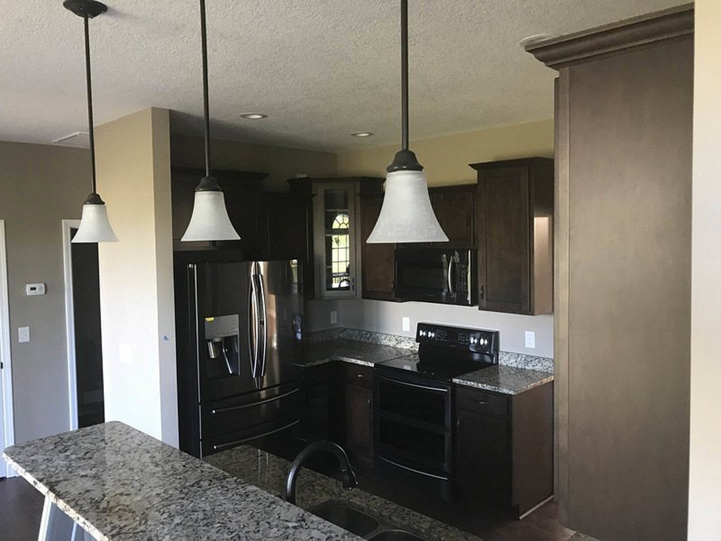 Kitchen with granite countertops, marble island, black refrigerator, black oven, black microwave, white cabinetry, stainless steel sink, modern light fixture, and neutral walls
