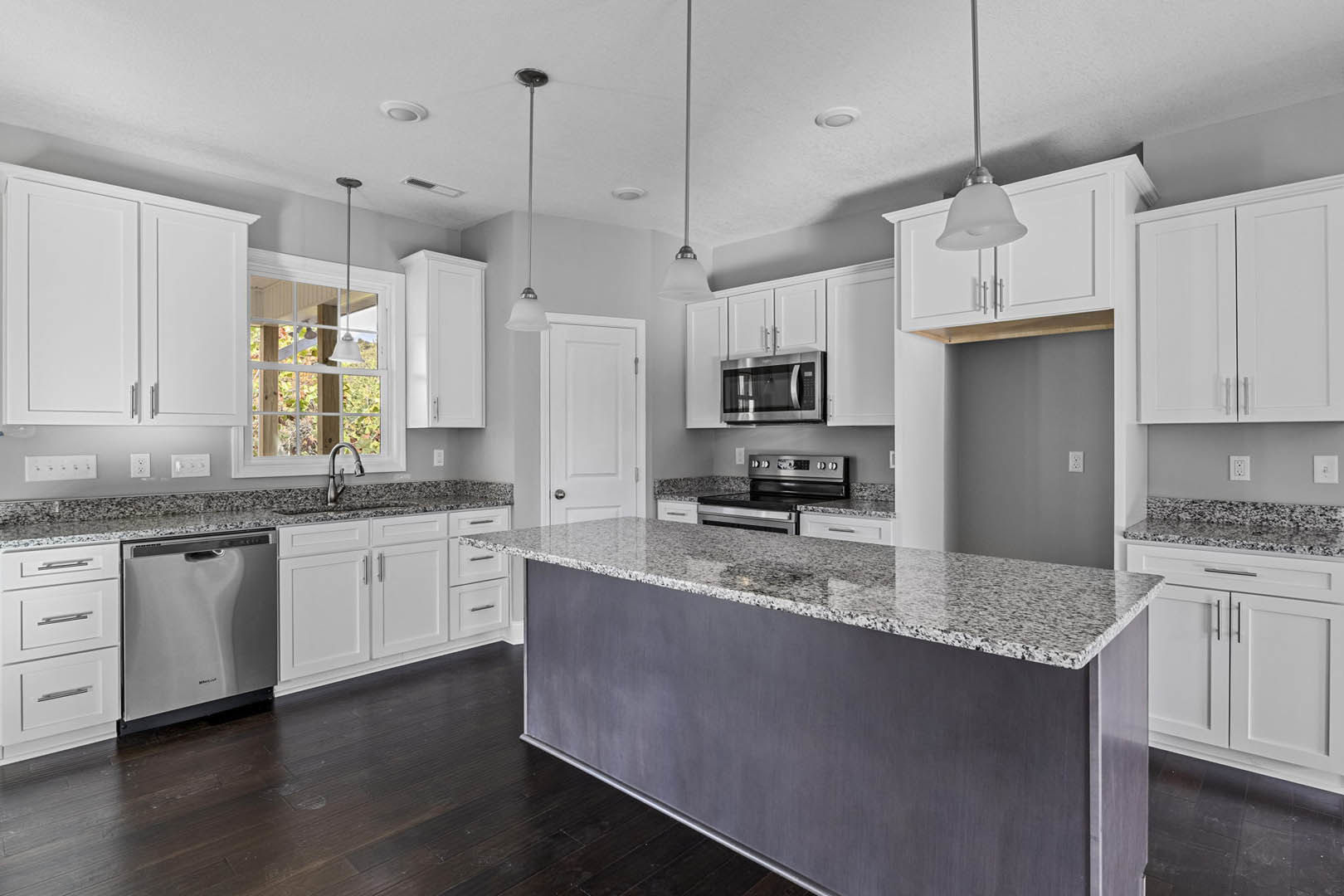Granite countertops and white cabinets in a kitchen with stainless steel appliances, including microwave, stove, dishwasher, and a chrome faucet over a sink.