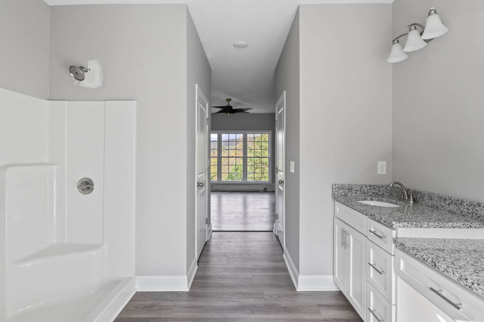 Modern bathroom featuring a freestanding white bathtub, rectangular sink with chrome faucet, dark wood cabinetry, marble countertop, three-bulb light fixture, large window