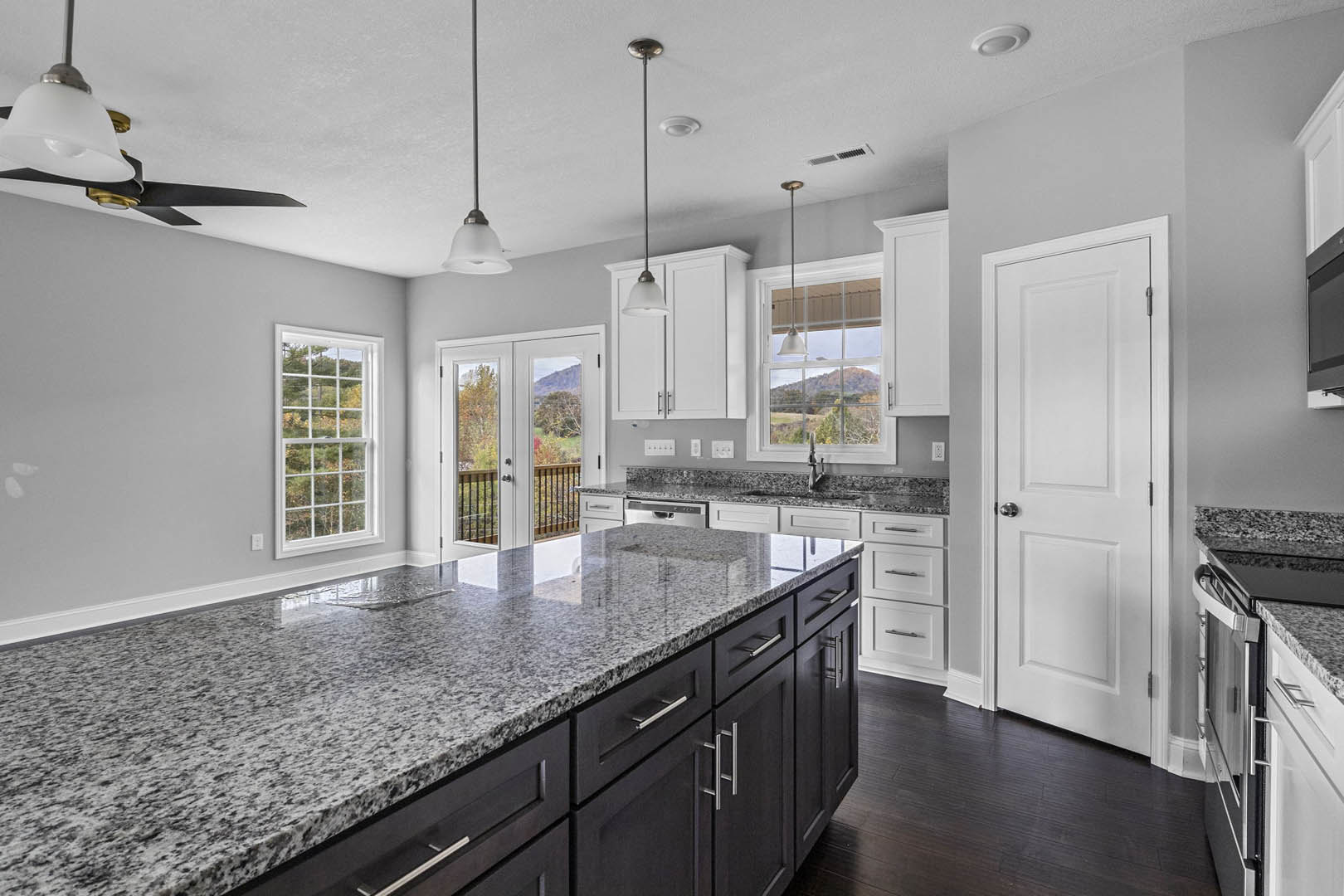 Granite countertops, white cabinetry, stainless steel appliances, and a large window with multiple panes in a modern kitchen