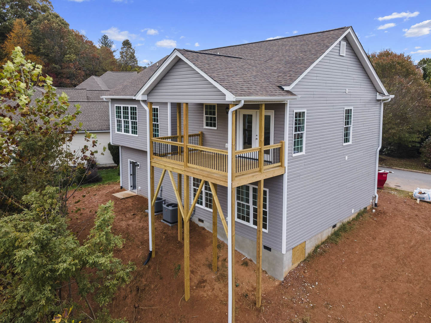 Two-story home with white siding, large balcony featuring metal railing, multi-pane windows, and a tree in the landscaped front yard