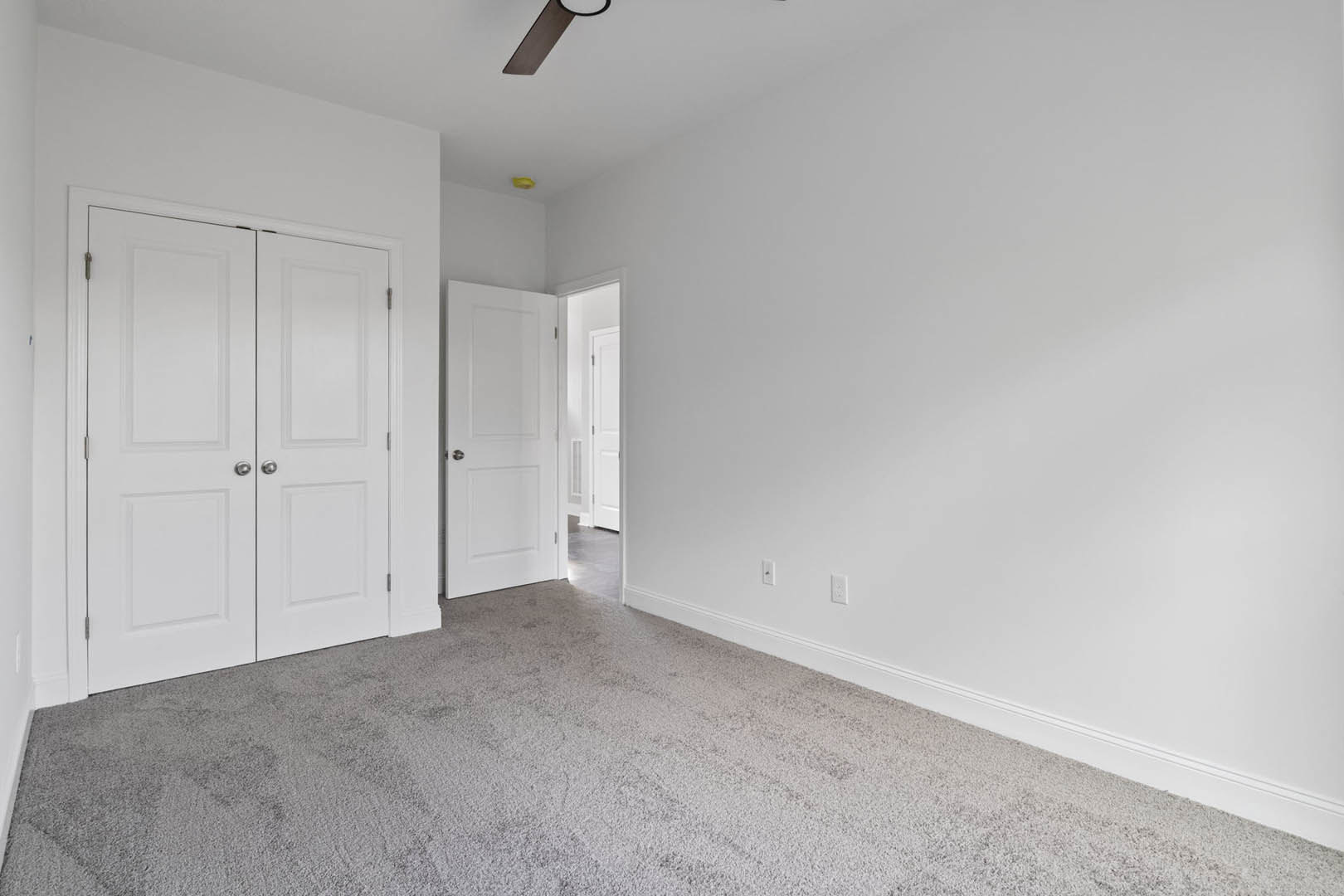 White-walled room with light carpet flooring, double white doors featuring silver handles, single white door with silver knob, smooth plaster ceiling