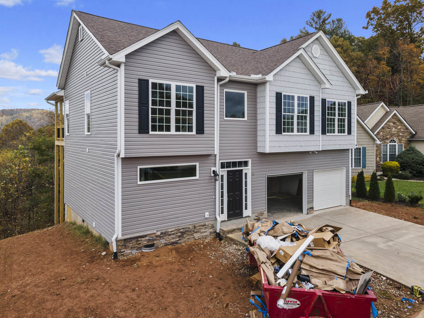 Two-story home with white siding, black door with white trim, attached garage, and driveway; red dumpster overflowing with cardboard and trash in front; Ronald Reagan Boyhood Home