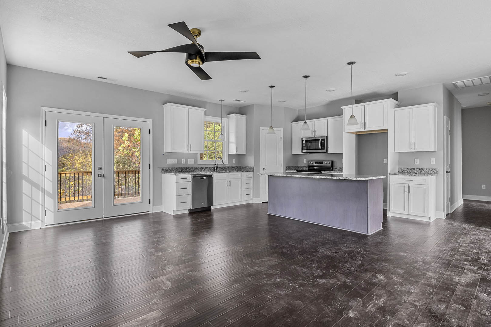 Open kitchen and dining area featuring dark wood laminate flooring, black-bladed ceiling fan, glass-paneled double doors, white cabinetry, stainless steel microwave, and stone