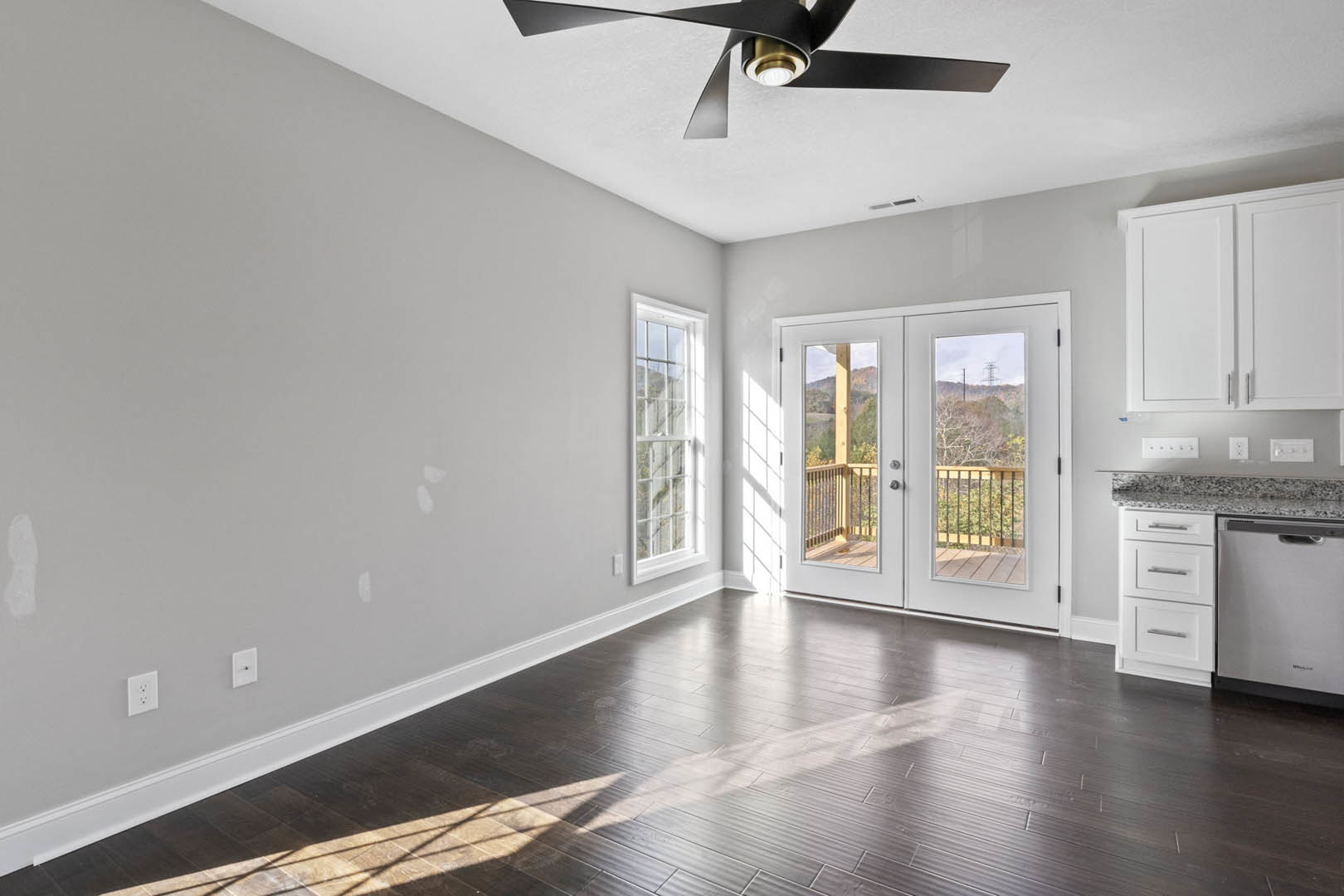 Dark wood flooring with white baseboards, ceiling fan with light fixture, double glass doors, white electrical outlet on wall, neutral painted walls