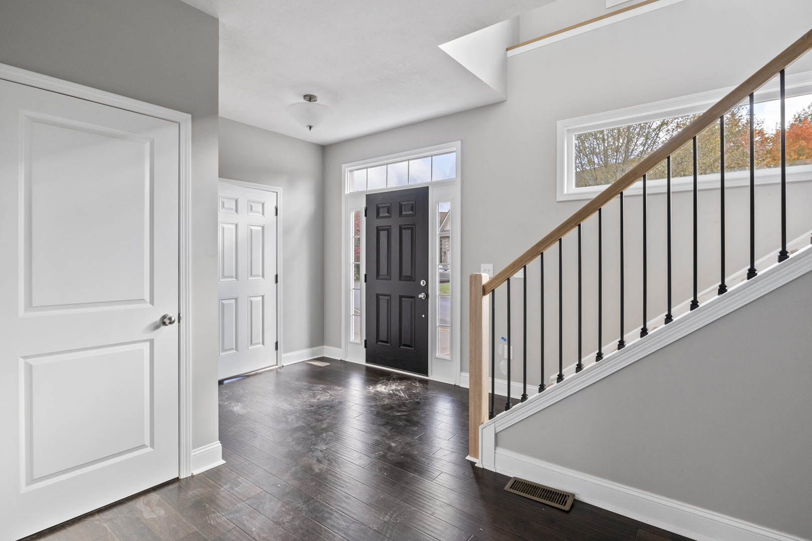 Hallway featuring light wood flooring, white walls with crown molding, a staircase with black metal railing, and a black paneled door