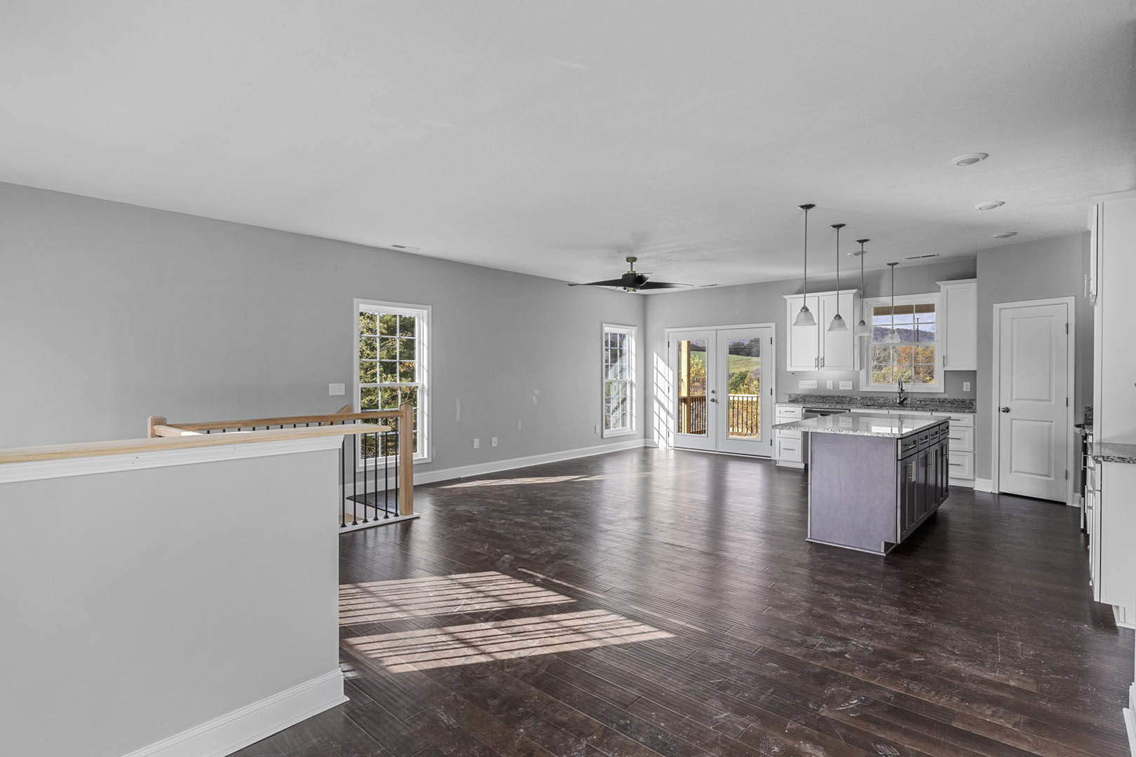 Spacious open floor plan featuring wood flooring, kitchen island with marble countertop, double glass-panel doors, white walls with railing, white door with silver knob, and white