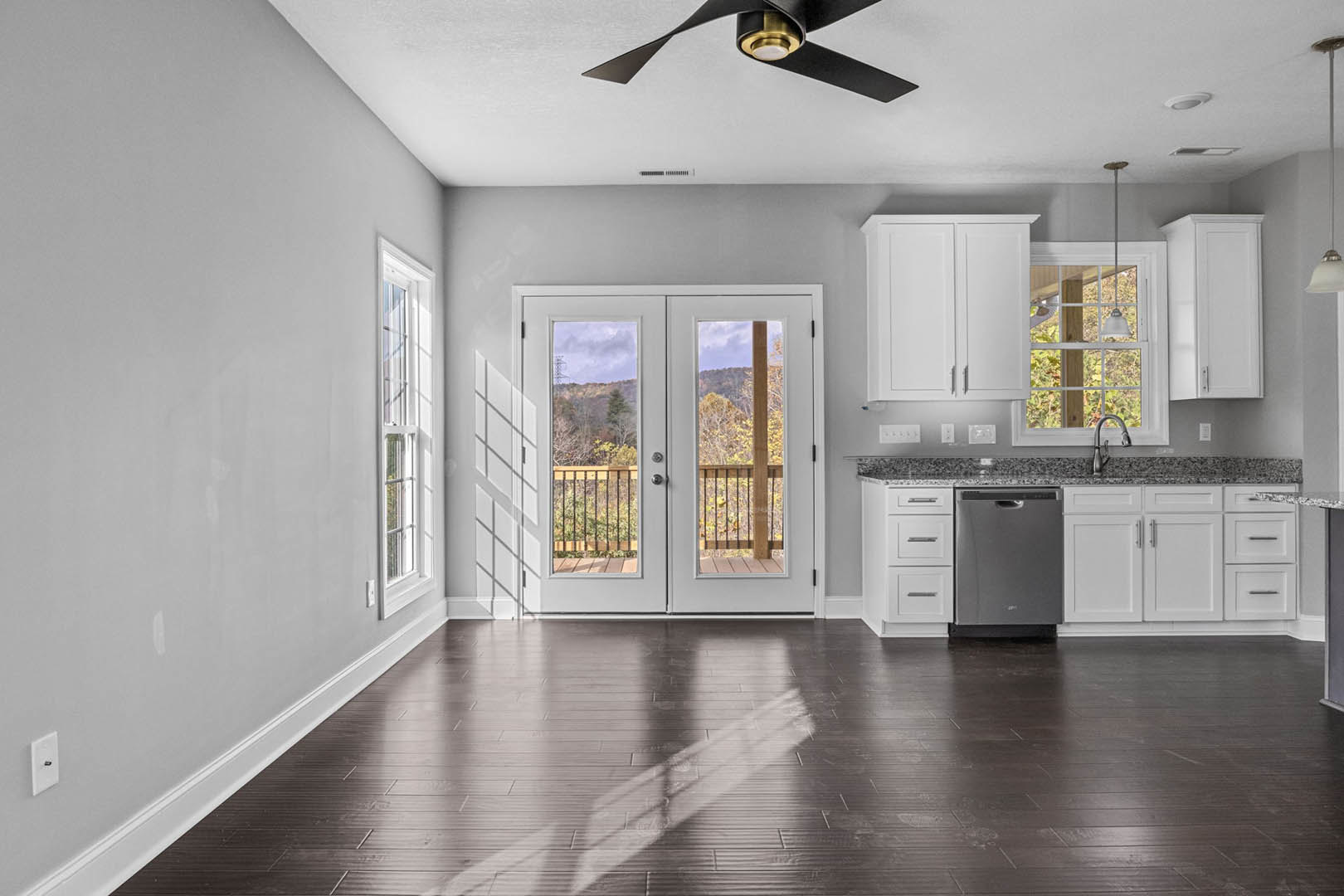 Modern kitchen with wood cabinetry, grey refrigerator, ceiling fan, and glass double doors opening to mountain views; polished wooden floor reflects a person, faucet and countertop
