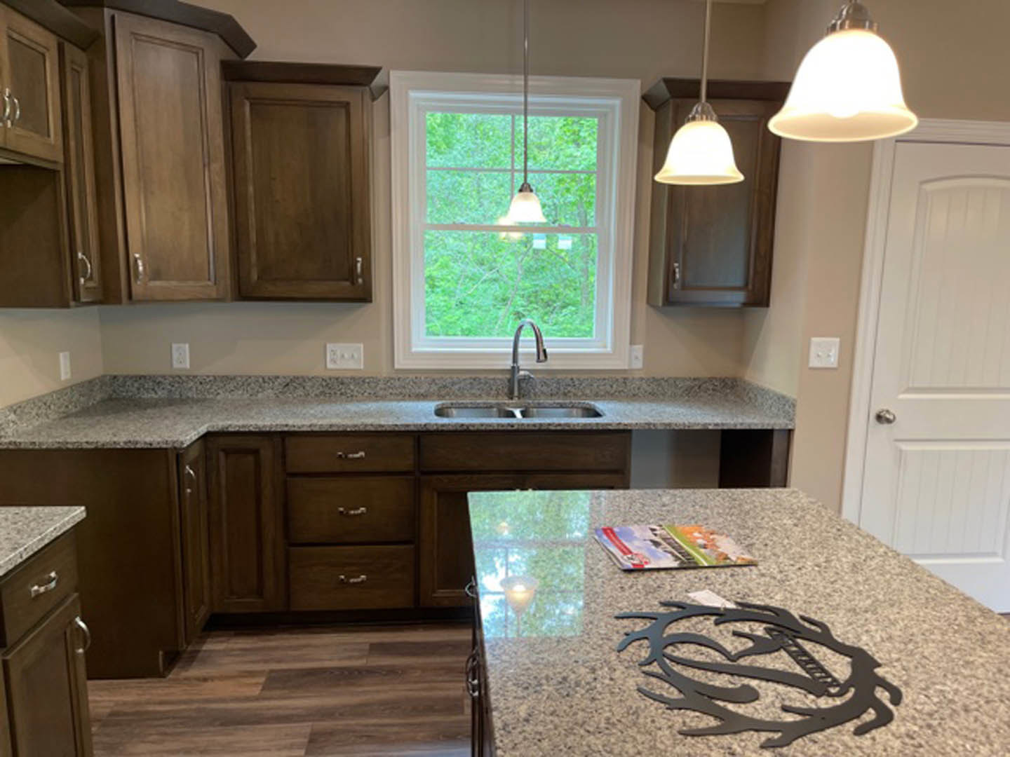 Granite countertops with undermount sink, white cabinetry, black metal art on marble counter, white light switch on wall, window with natural light, blurred book in foreground