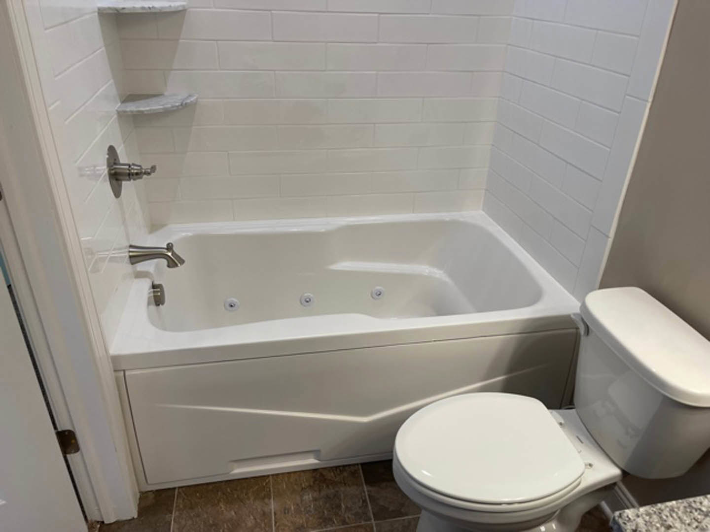 White freestanding bathtub beside matching toilet, glossy white tile walls, chrome faucet, minimalist bathroom design