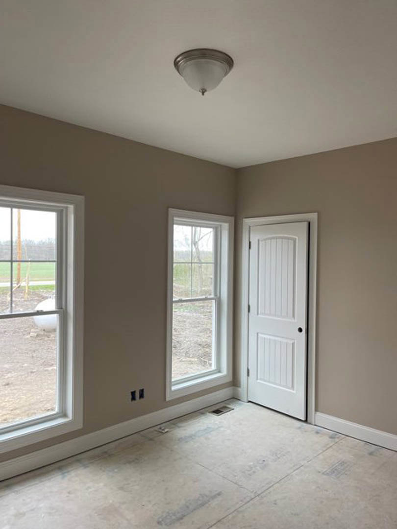 White paneled door with black hardware, two large windows showing playground and outdoor view, light fixture on ceiling, pale plaster walls, vent in corner of light wood floor