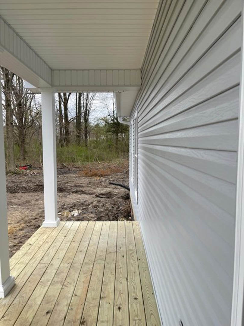 Wood deck porch with white siding wall, white ceiling paneling, and white post; window visible on house exterior