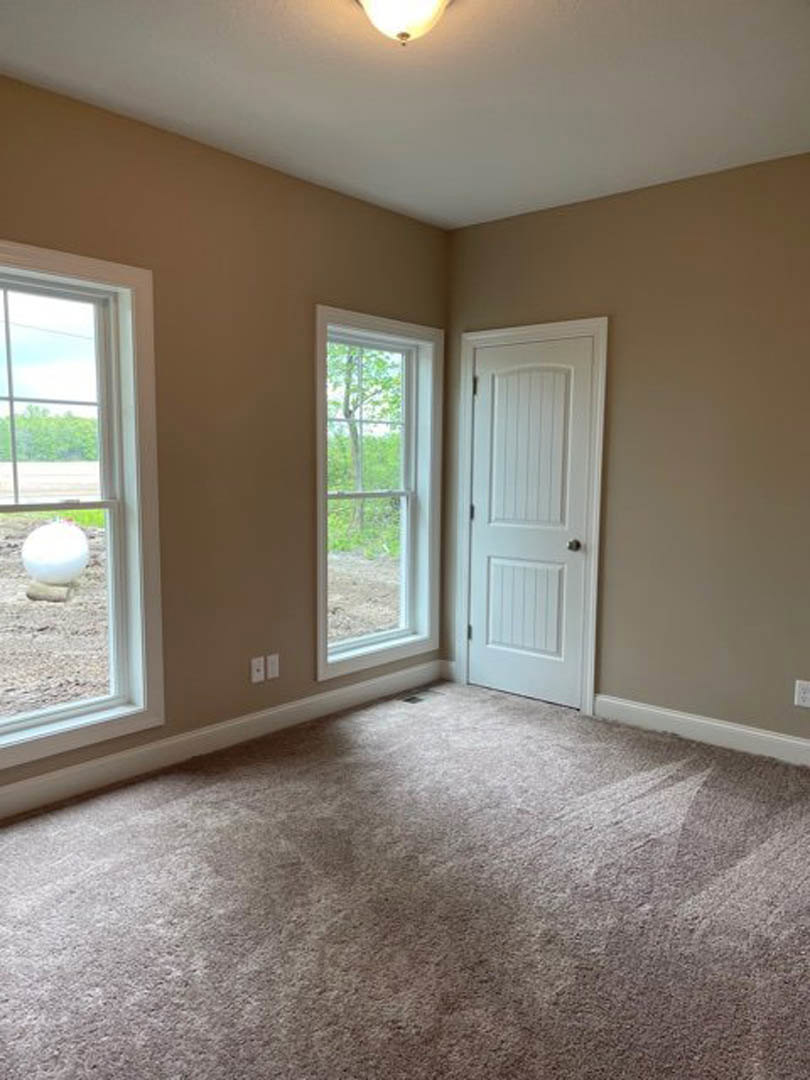 Laminate flooring room with white plaster walls, white door featuring a silver knob, two windows—one showing trees outside, the other containing a white object—plus a white ball