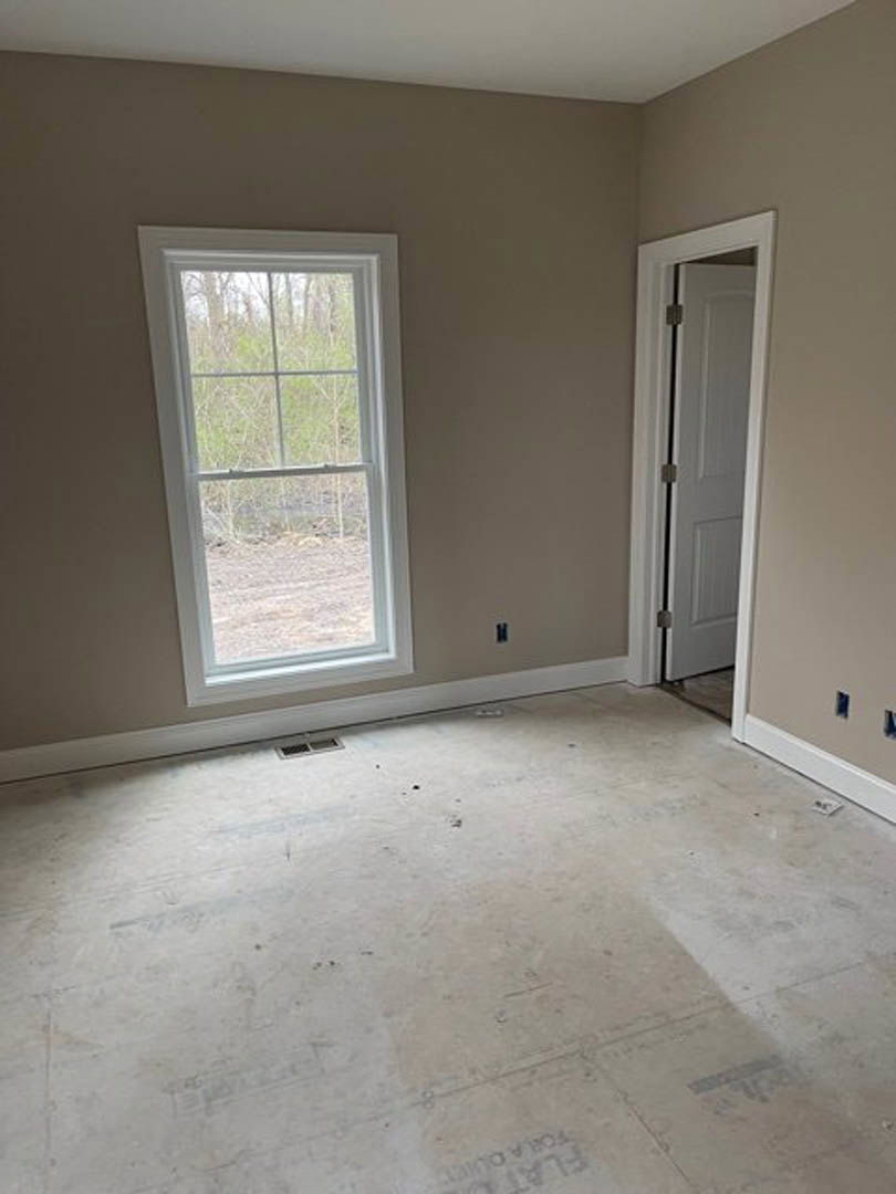 Bright room featuring a large window with tree views, white door with visible hinge, tile flooring, plaster walls, and white ceiling accented by a brown border
