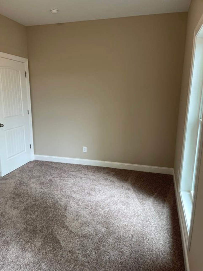 White paneled door with silver doorknob, beige carpeted floor, white baseboards, and a window set in a plastered wall.