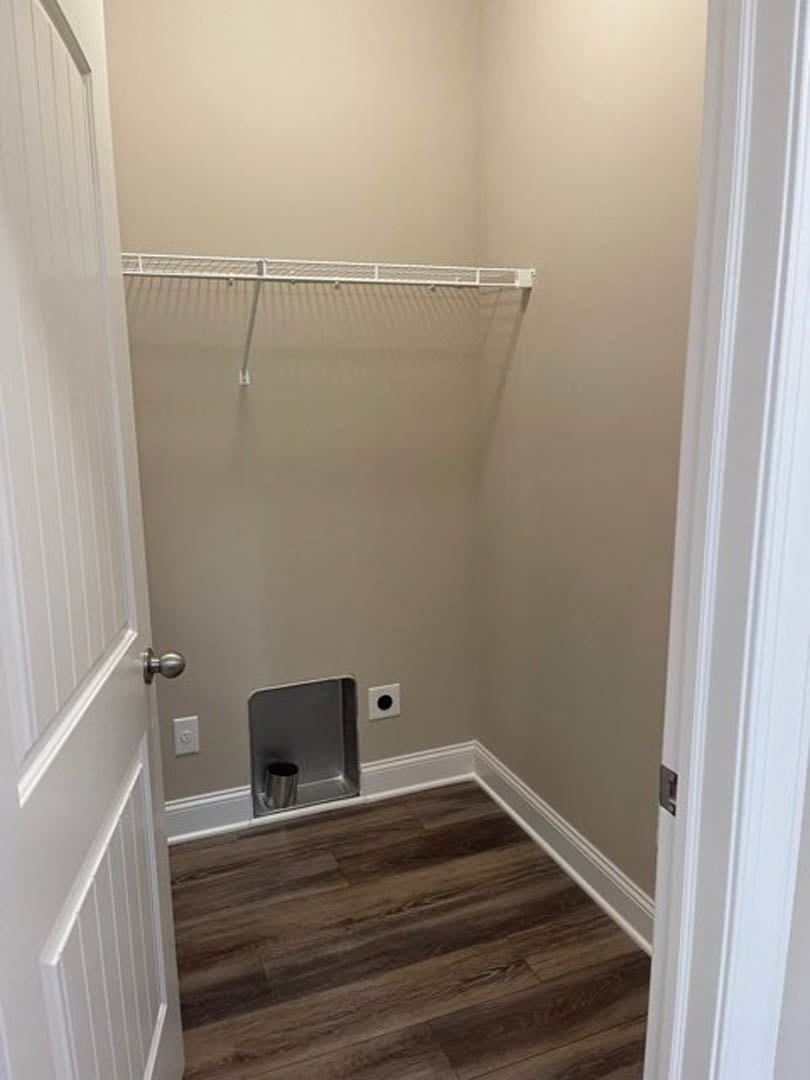 Walk-in closet with wood flooring, white trim, built-in metal trash bin, white shelving and hanging bar, and a small dog door in the lower part of a white door