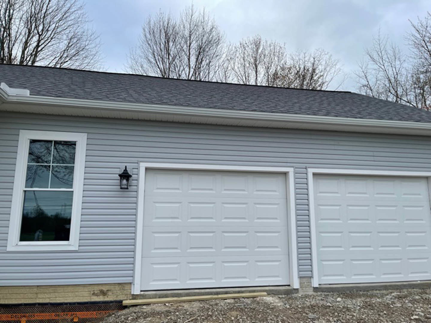 Two white garage doors set in grey siding, each with a white-framed window above and exterior wall lights beside the doors.