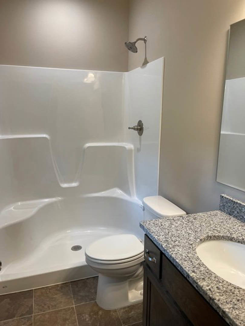 Modern bathroom featuring a glass-enclosed shower, white porcelain sink with chrome faucet, adjacent toilet, light-colored tile walls, and a large wall mirror above the vanity