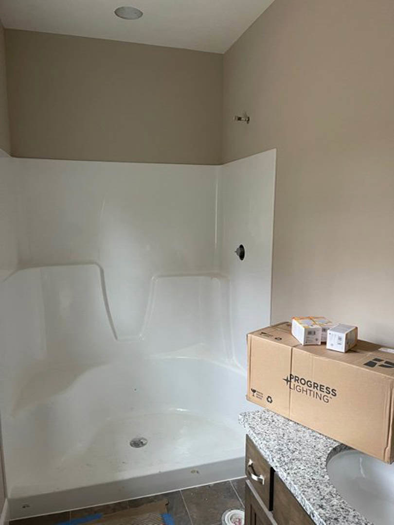 White bathroom with a rectangular sink, countertop holding a white box with black text, and glass-enclosed shower with chrome fixtures