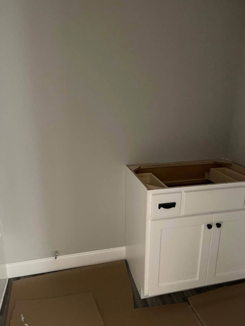 White shaker-style cabinet with single drawer and silver handle set against light-colored wall and hardwood floor