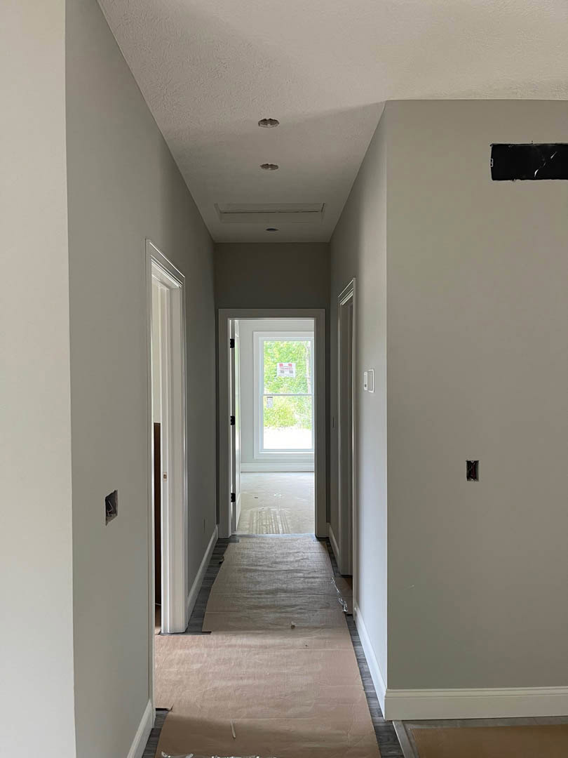 White hallway with carpeted floor, brown paper runner, white door featuring a sign, black rectangular object on wall, window with sign, plaster walls and ceiling