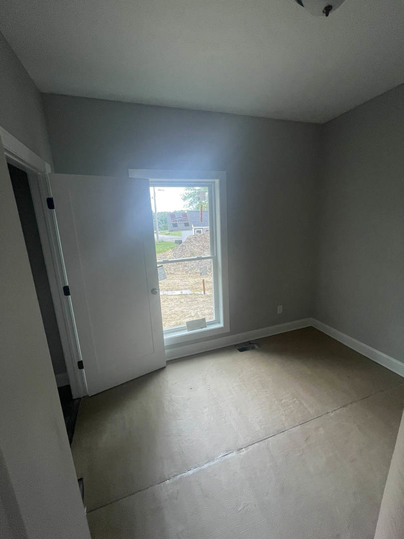 Concrete floor with central drain, white plaster walls, white door with metal handle and sign, large window allowing daylight into minimalist room