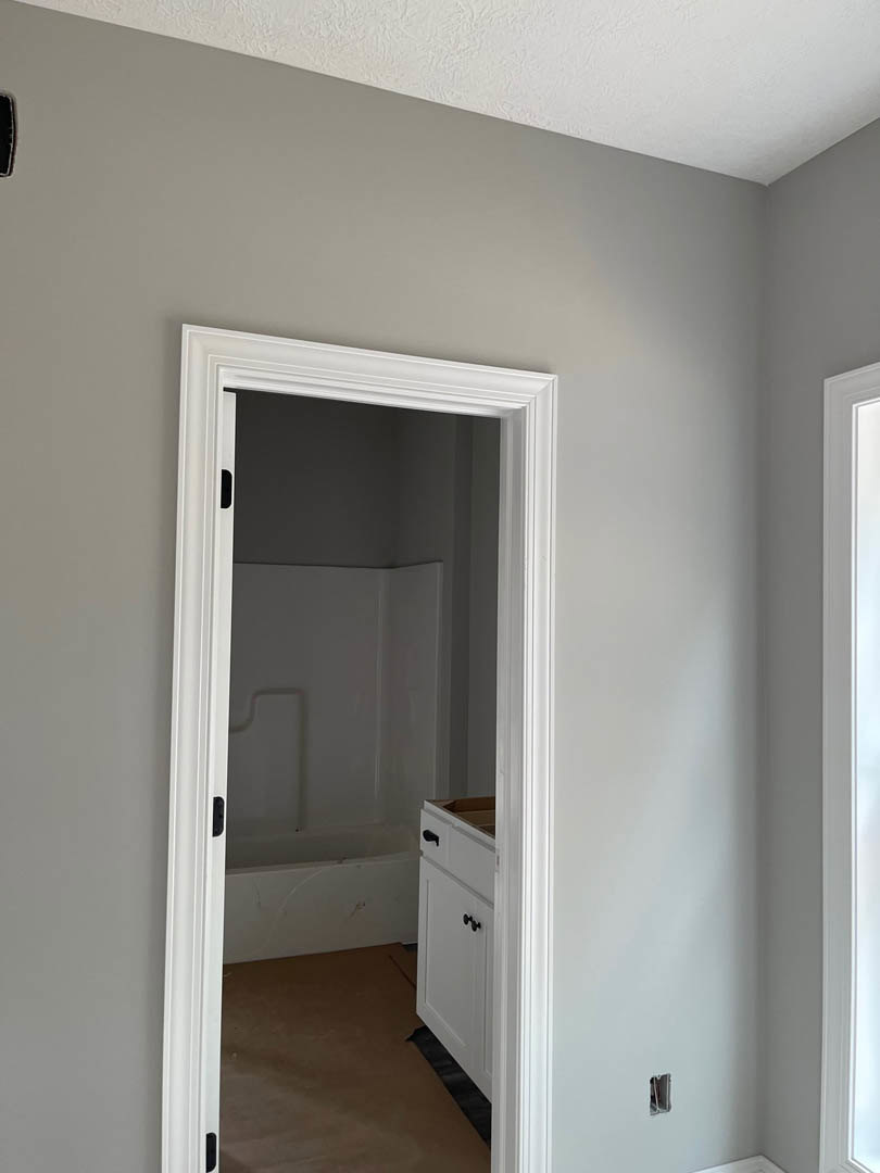 White plaster walls and ceiling, brown flooring with protective paper, black floor mat, white bathroom door, visible pipe, bathtub, and sink.