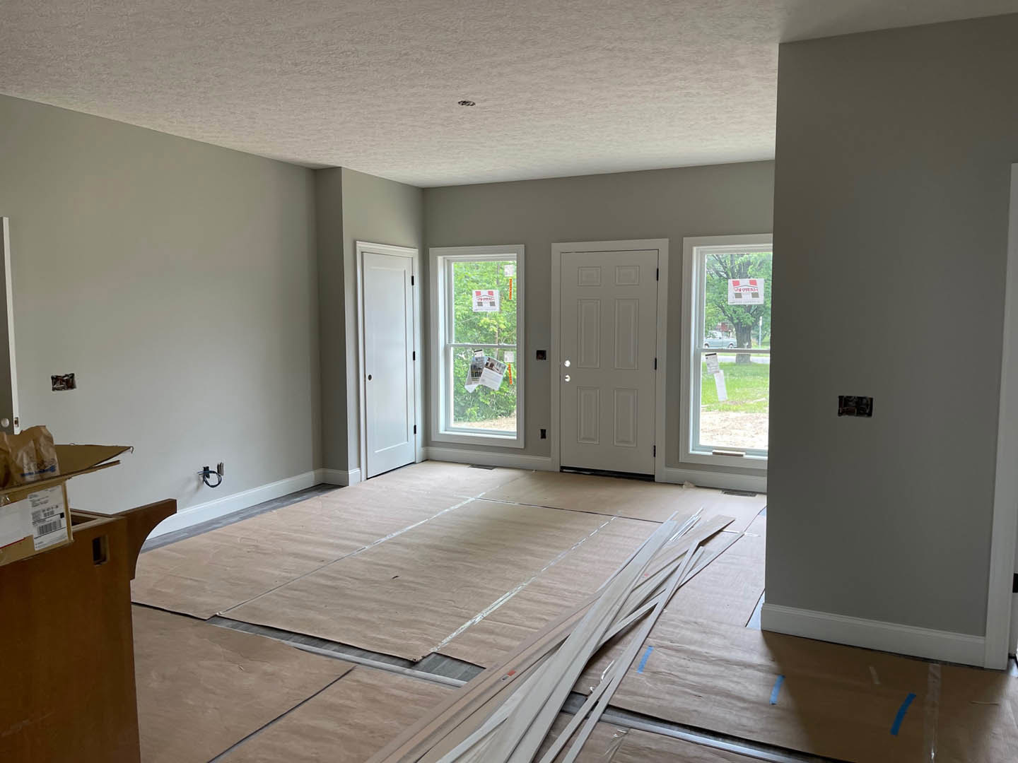 Room with two white doors featuring black handles and round knobs, laminate wood flooring, window with papers and sign attached, cardboard on the floor, white walls