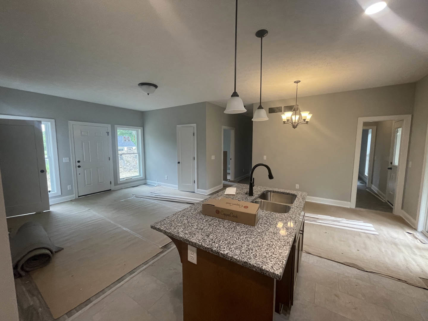 Open kitchen with white cabinetry, marble countertops, stainless steel sink, kitchen island featuring a brown box, modern chandelier, white door with black knobs, tile flooring
