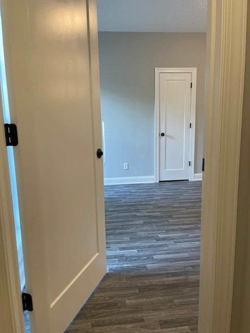 White paneled door with black knob set in a room with light wood flooring and white walls