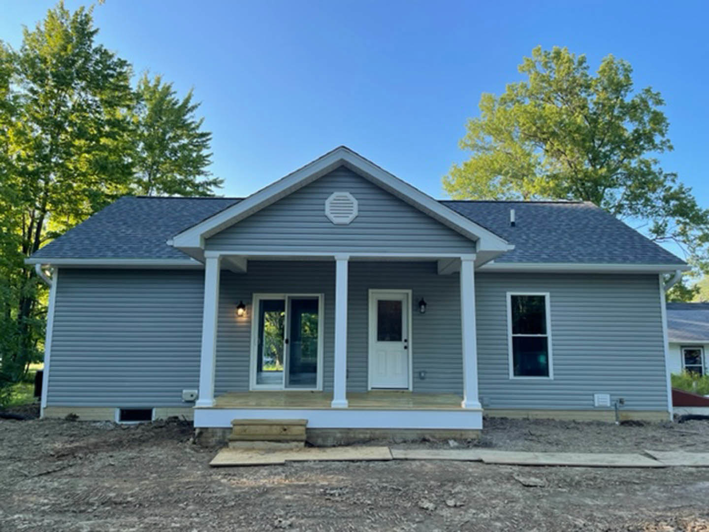 Blue siding house with two porches, white vent, white door with window, open window, and surrounding trees under clear sky