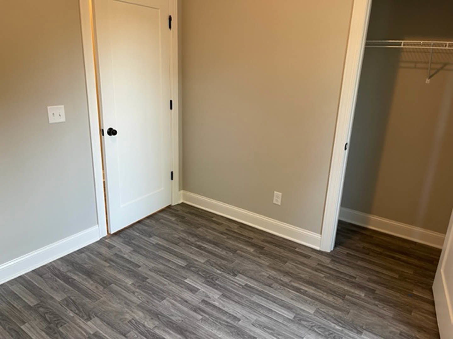 Wood flooring with white baseboards, white door with matching trim, white wall featuring a light switch