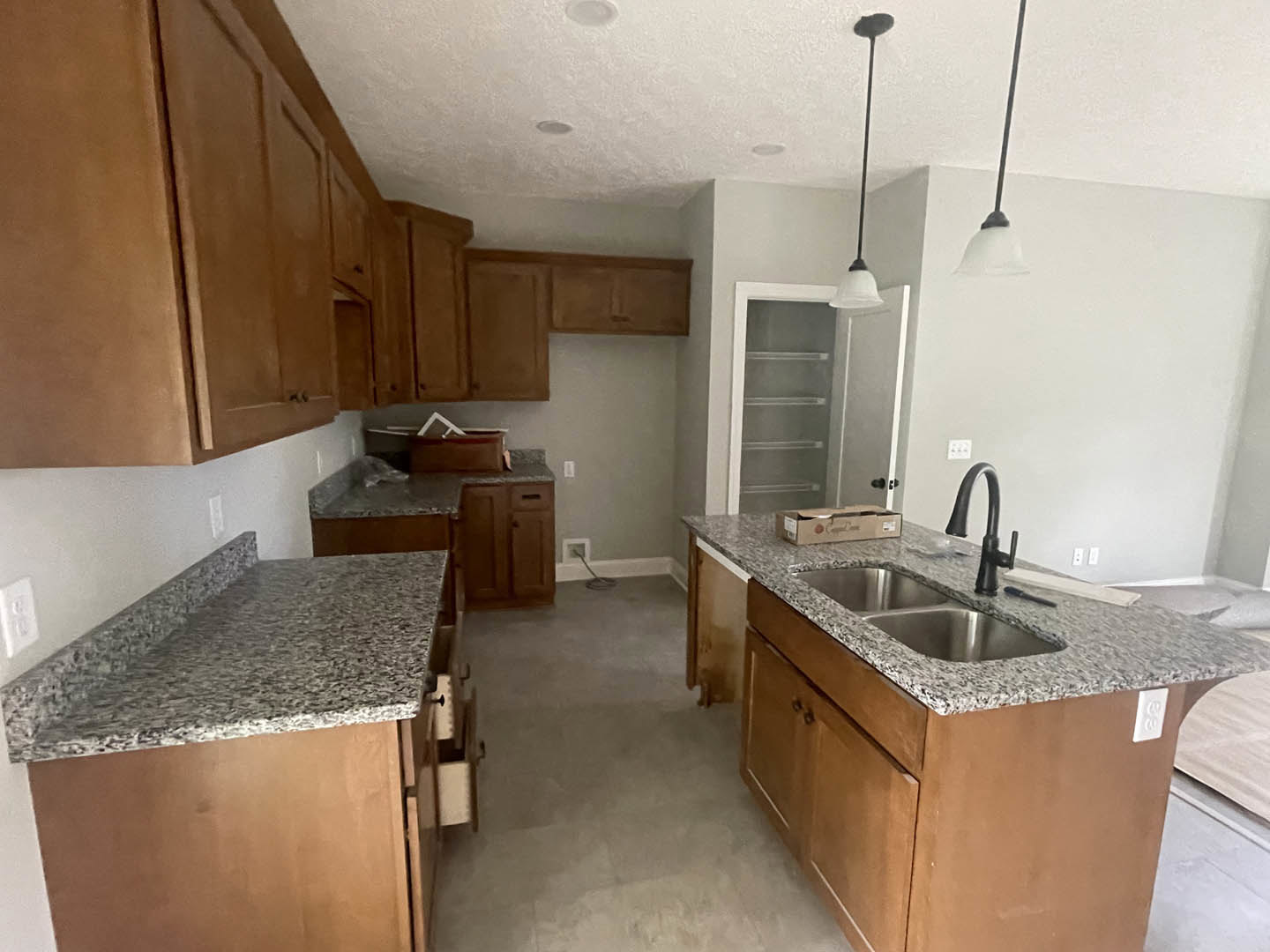 Granite kitchen island with undermount sink and matte black faucet, surrounded by white cabinetry and stainless steel appliances