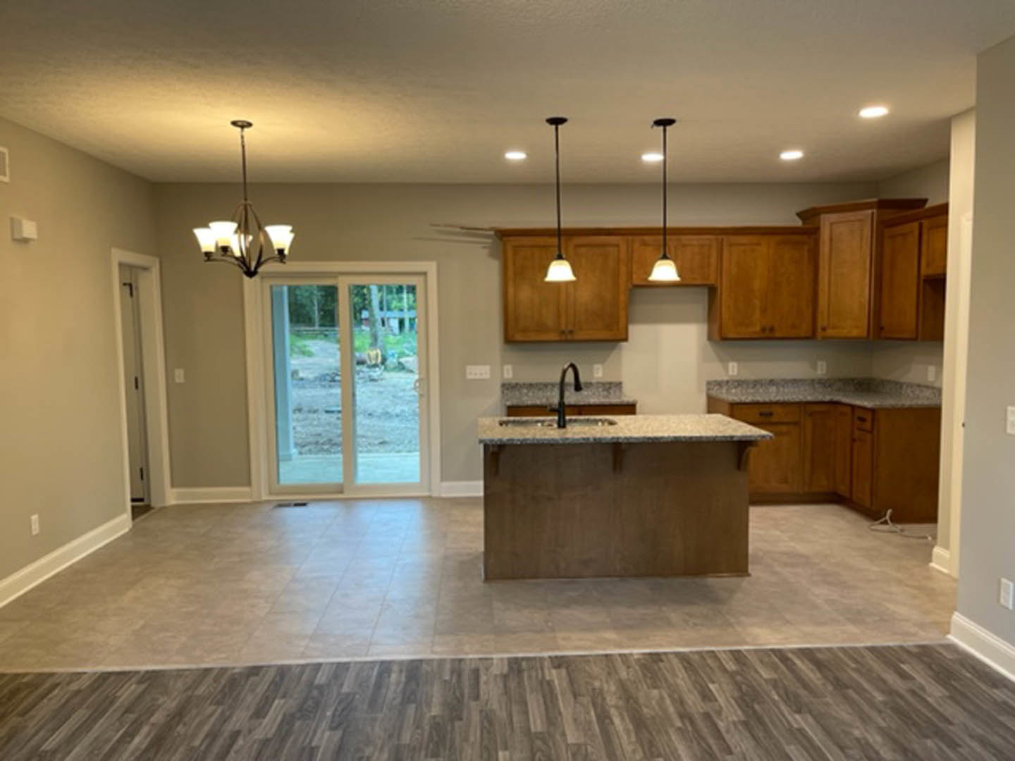 Spacious kitchen featuring a large central island with stone countertop, built-in sink, white cabinetry, wood flooring, glass door opening to backyard, modern chandelier, and