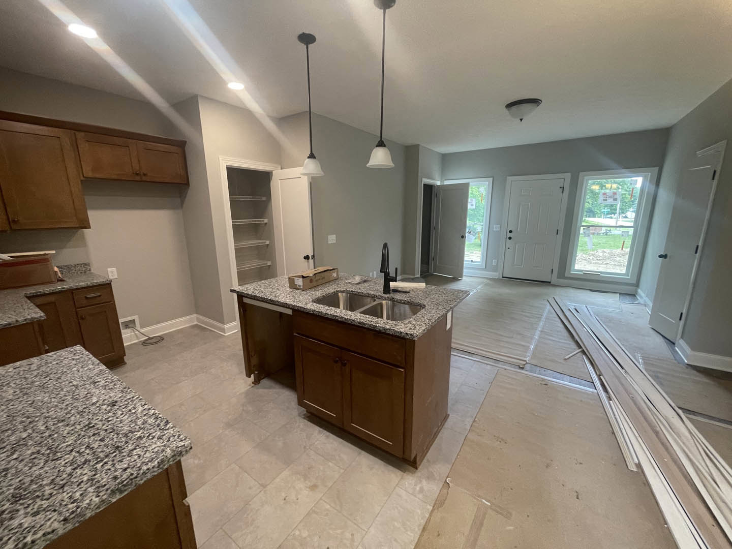 Granite kitchen island with undermount sink, speckled black and white countertop, white cabinetry with black hardware, pendant light fixture, tile flooring