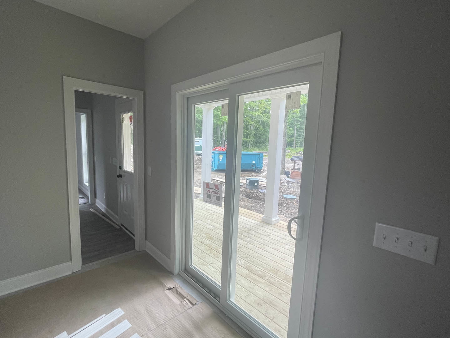 Glass door with white frame set in a blue wall, row of switches on adjacent wall, hallway with white door and white sign featuring black text