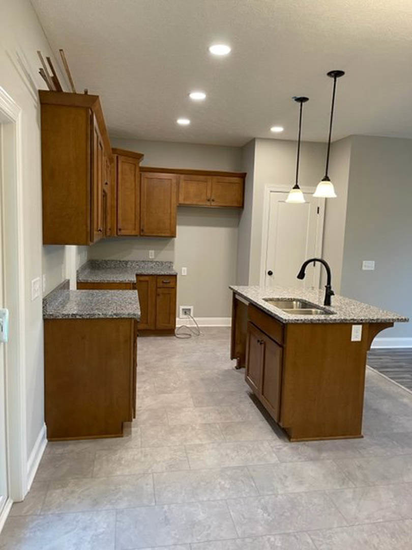 Granite countertops and wood cabinets in a kitchen with marble flooring, kitchen island featuring a sink, cord plugged into wall outlet, close-up of light fixture and wood surface